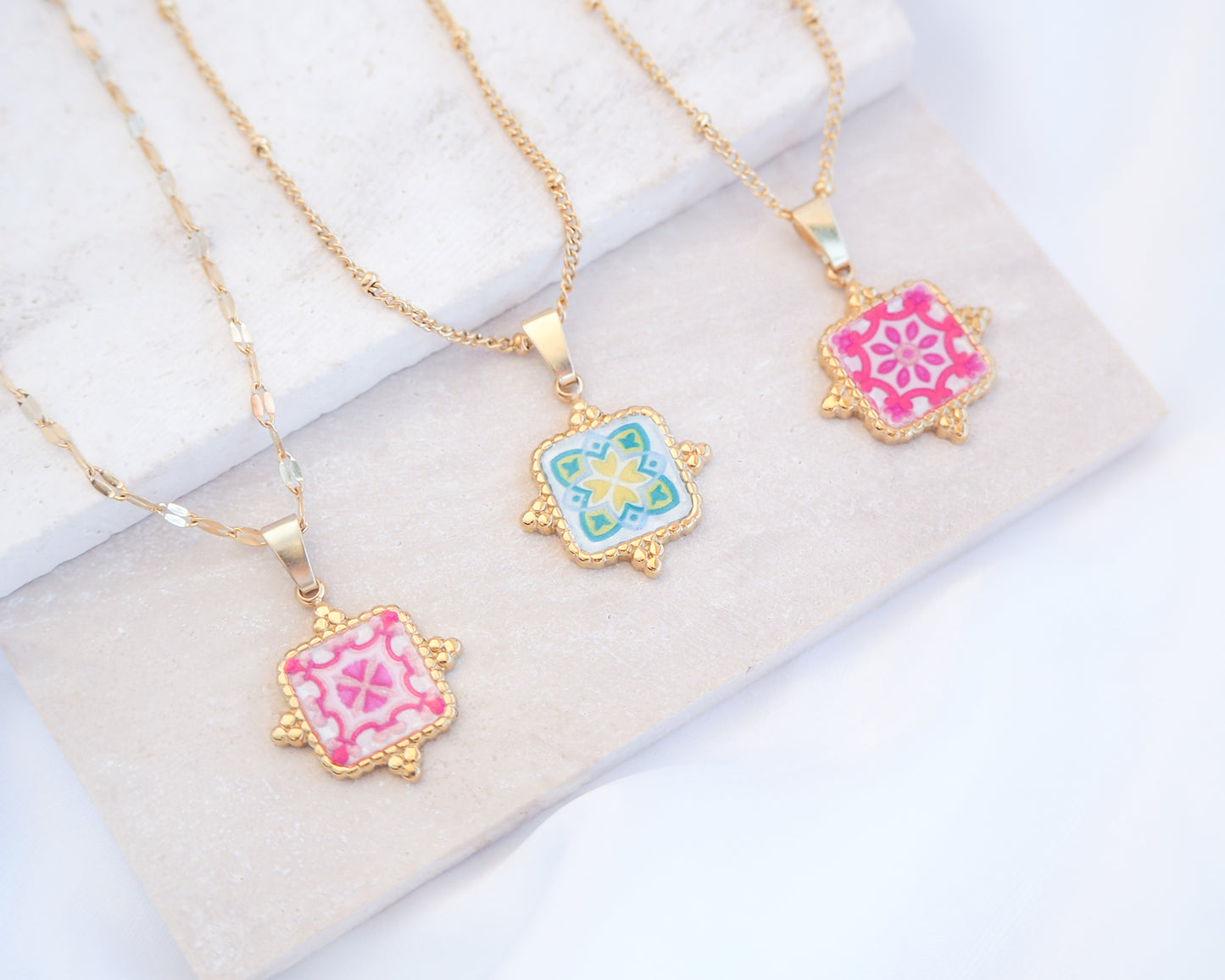 Close up of Gold Portuguese Tile Square Necklaces Pink and Green on stone displayed. Made with 18k gold stainless steel and white pink green yellow mosaic pendant inspired by the Portuguese Azulejo design pattern. 