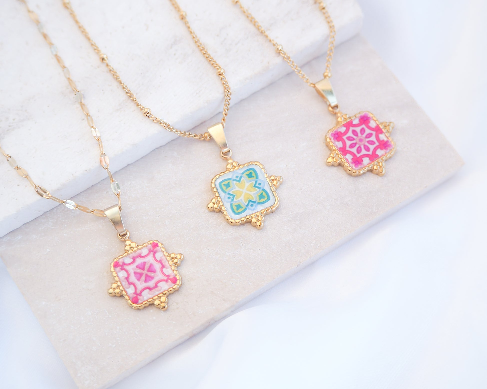 Close up of Gold Portuguese Tile Square Necklaces Pink and Green on stone displayed. Made with 18k gold stainless steel and white pink green yellow mosaic pendant inspired by the Portuguese Azulejo design pattern. 