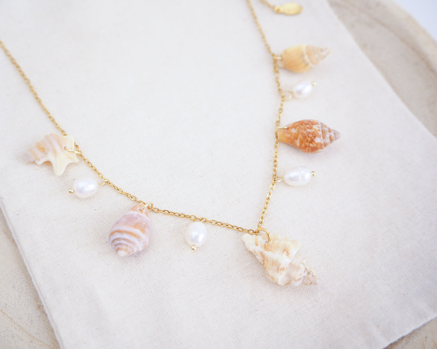 Necklace with seashells and pearls on a white surface. Portuguese Shell Pearl Charm Necklace with tiny shells from Portugal. Mediterranean cone shell, pelican foot shell, rustic dove shell, netted dog whelk shell, sting winkle shell. Ivory white Freshwater pearls