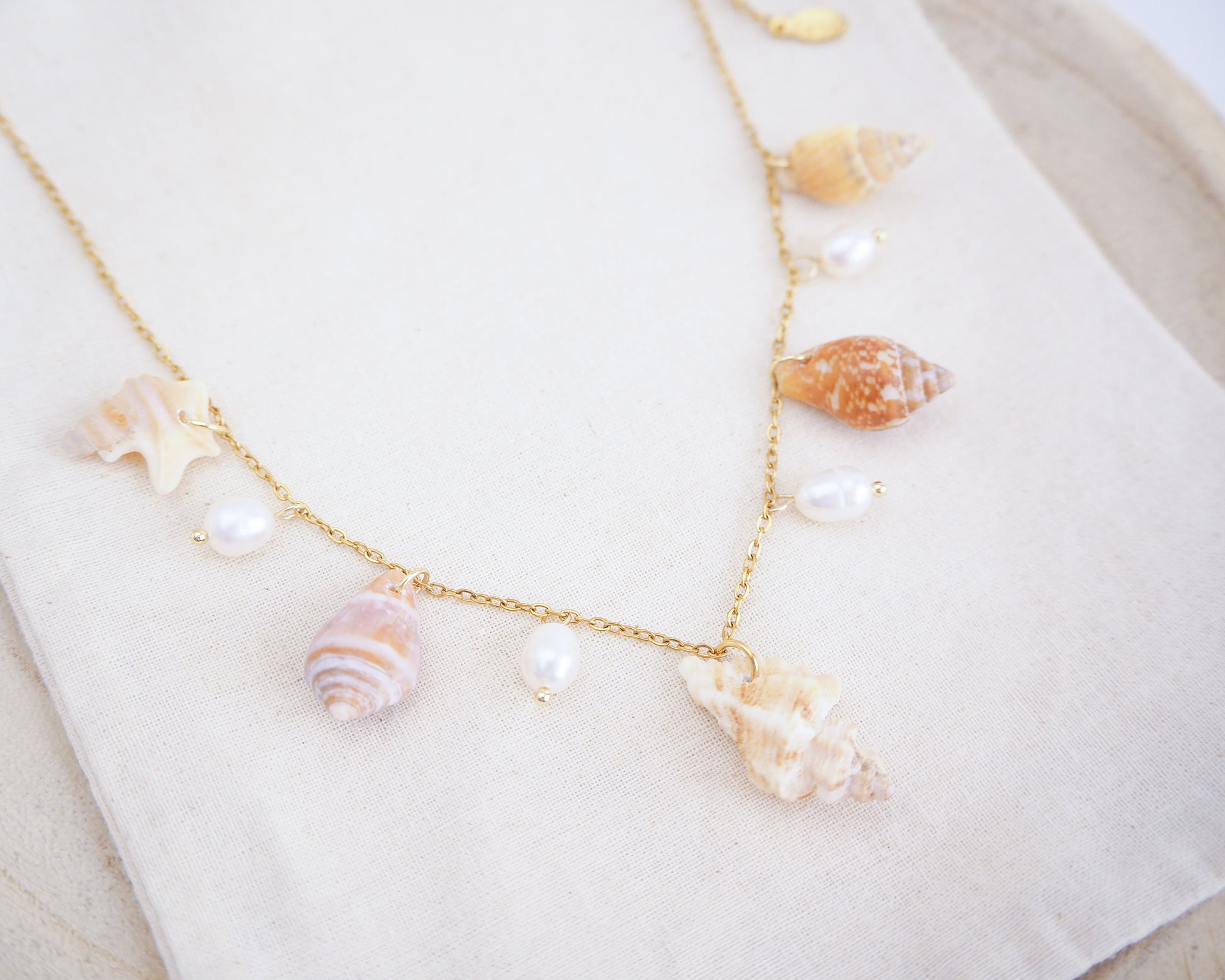 Necklace with seashells and pearls on a white surface. Portuguese Shell Pearl Charm Necklace with tiny shells from Portugal. Mediterranean cone shell, pelican foot shell, rustic dove shell, netted dog whelk shell, sting winkle shell. Ivory white Freshwater pearls
