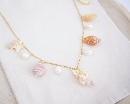Necklace with seashells and pearls on a white surface. Portuguese Shell Pearl Charm Necklace with tiny shells from Portugal. Mediterranean cone shell, pelican foot shell, rustic dove shell, netted dog whelk shell, sting winkle shell. Ivory white Freshwater pearls
