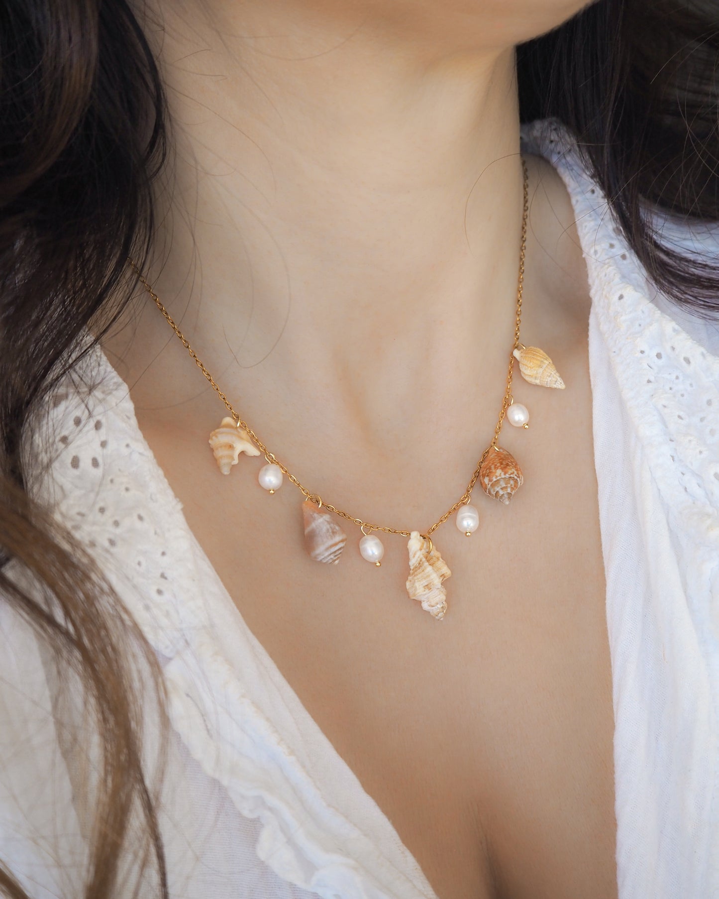 Necklace with shell and pearl pendants on a model wearing a white lace top. Portuguese Shell Pearl Charm Necklace with tiny shells from Portugal. Mediterranean cone shell, pelican foot shell, rustic dove shell, netted dog whelk shell, sting winkle shell. Ivory white Freshwater pearls