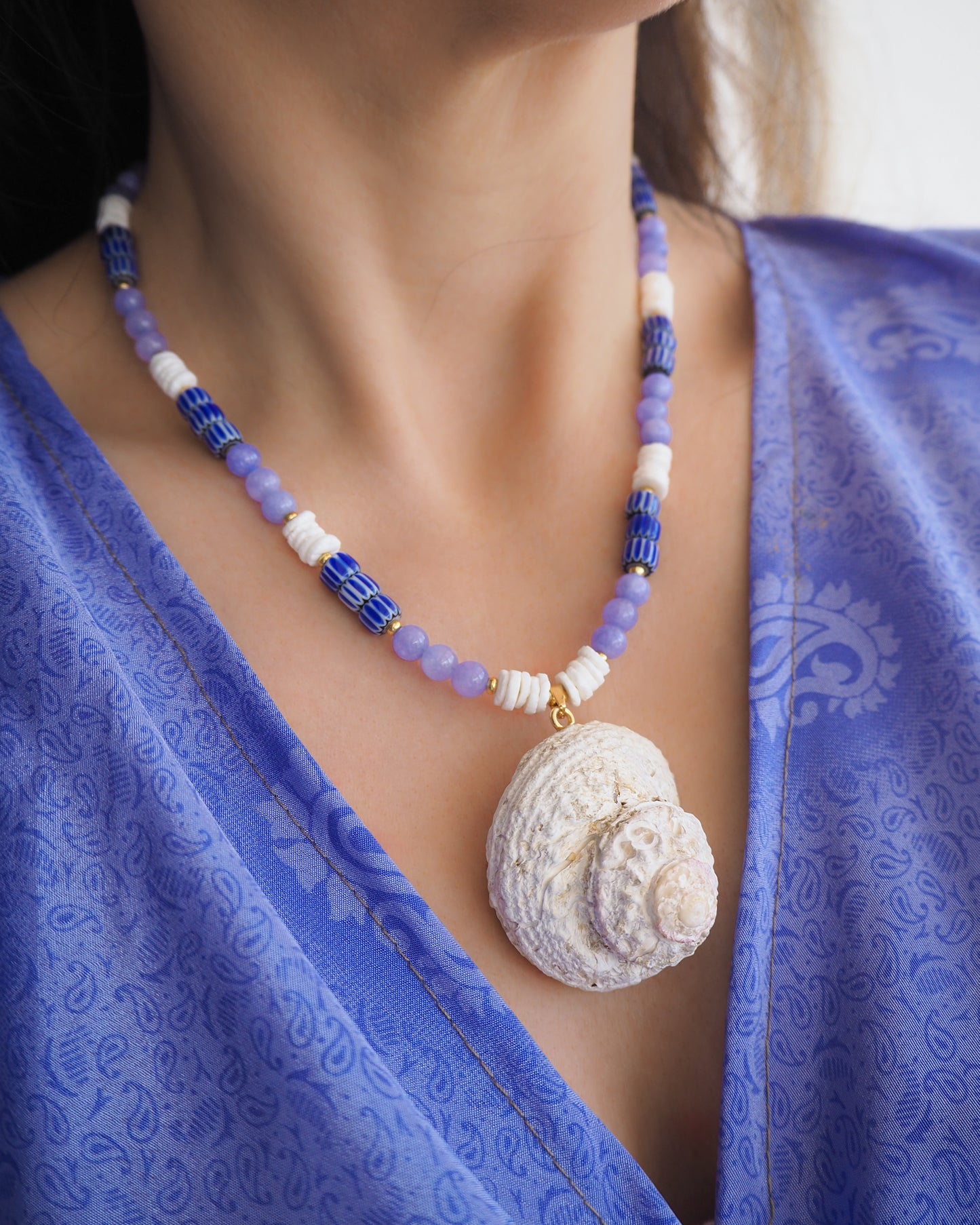 Model wearing a necklace with a big star shell paired with blue angelite gemstone beads, blue striped beads and white shell beads. The shell is a rough star shell from Portugal and is about 5 cm. The color of the shell is ivory white.