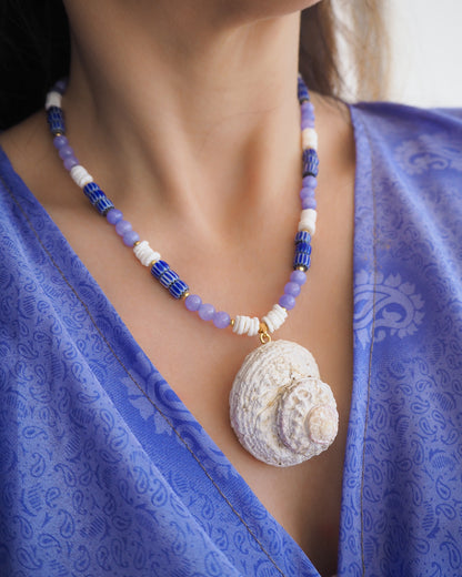 Model wearing a necklace with a big star shell paired with blue angelite gemstone beads, blue striped beads and white shell beads. The shell is a rough star shell from Portugal and is about 5 cm. The color of the shell is ivory white.