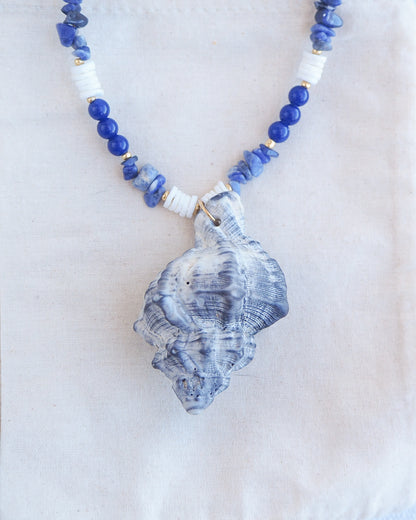 Front view close up of handmade necklace with a big grey murex shell paired with blue sodalite gemstone beads and white shell beads. The shell is a banded dye murex shell from Portugal and is about 8 cm. The color of the shell is grey.