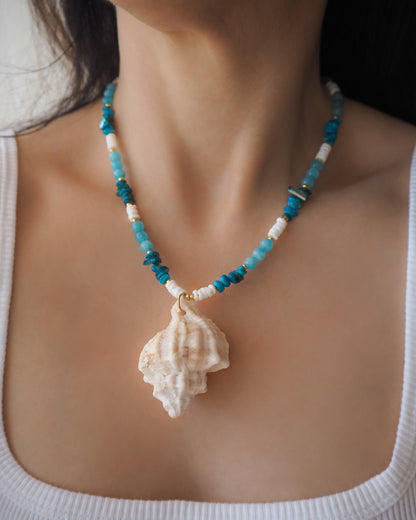 Model wearing a necklace with a big murex shell paired with aquamarine gemstone beads and white shell beads. The shell is a banded dye murex shell from Portugal and is about 6 cm. The color of the shell is ivory bege.