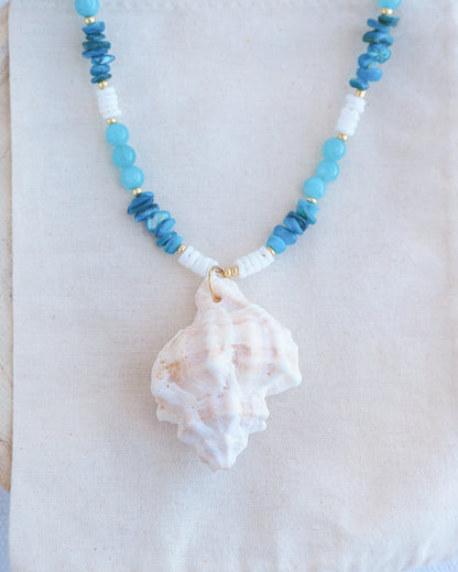 Necklace with blue and white beads and a shell pendant on a white background. Front view of a necklace with a ivory murex shell paired with aquamarine gemstone beads and white shell beads. The shell is a banded dye murex shell from Portugal and is about 6 cm. The color of the shell is ivory bege.