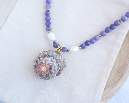 Necklace with purple beads and a shell pendant on a white background. A necklace with a big star shell paired with purple amethyst gemstone beads  and freshwater pearls. The shell is a rough star shell from Portugal and is about 4 cm. The color of the shell is kaki grey white.