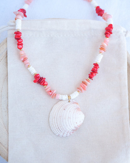 Front view of Necklace with shell pendant and coral-colored beads on a white fabric background. a necklace with red, pink, and white beads and a shell pendant on a beige surface. Big venus shell paired with red coral stones and white shell beads. The shell is a Warty Venus Clam shell from Portugal and is about 6 cm. The color of the shell is ivory bege.