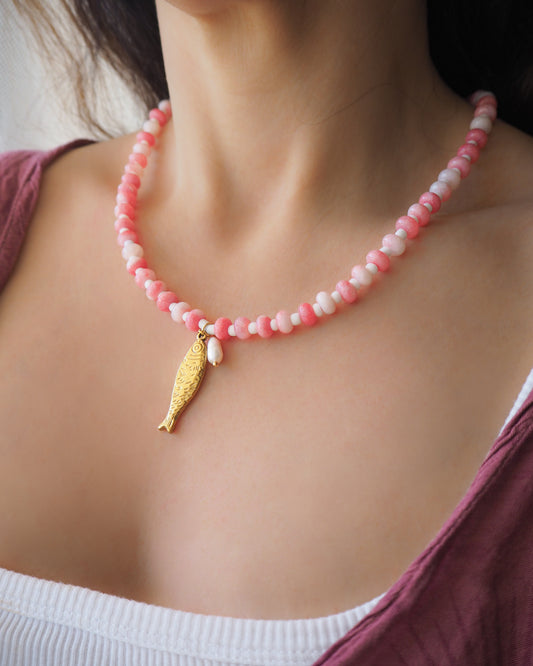 Model wearing a necklace with pink and white beads and a gold sardine fish pendant and freshwater pearl bead on a person wearing a white top. The necklace is made with seed beads and freshwater pearls and a big gold sardine fish The sardine fish pendant is made of 18k gold stainless steel. 