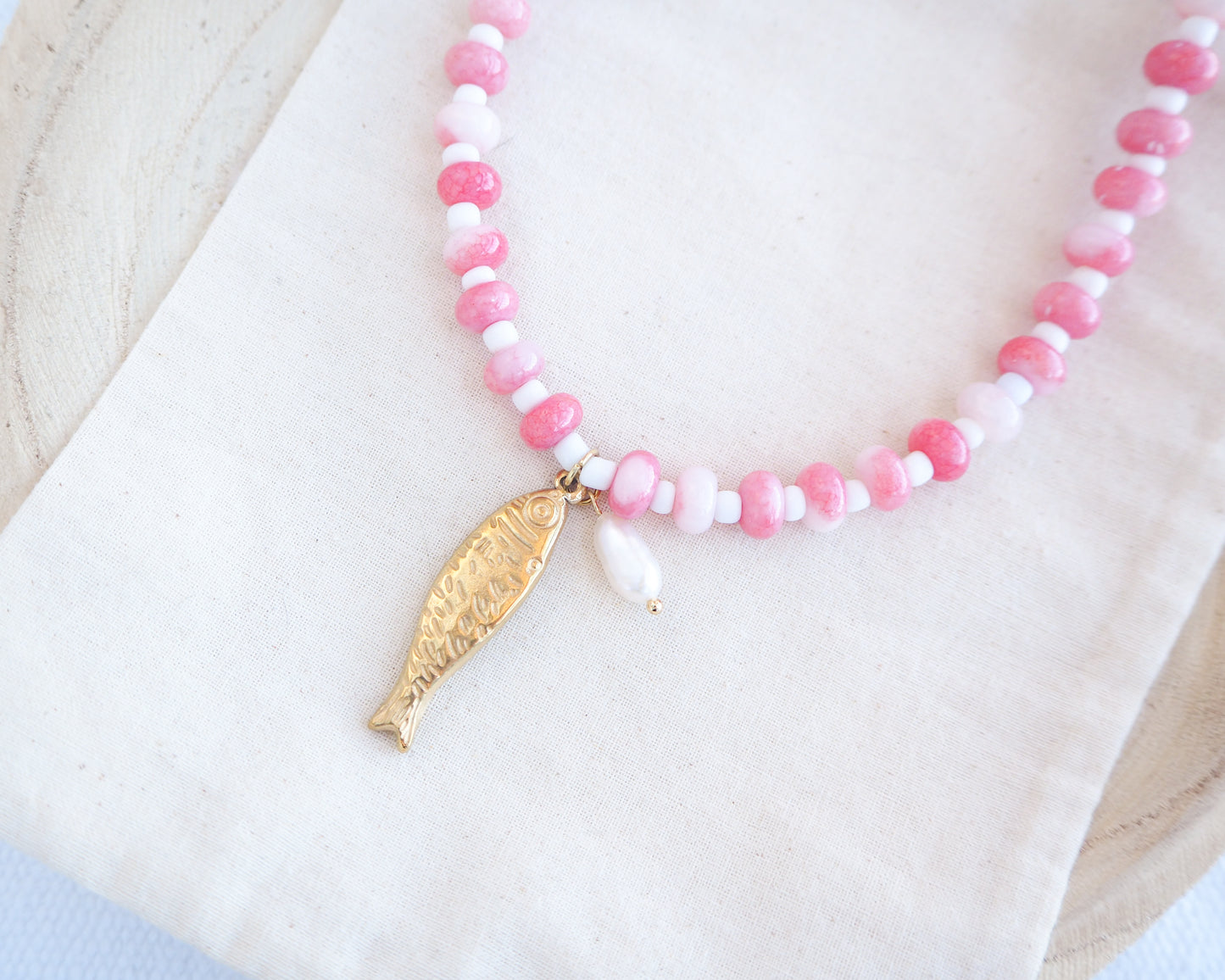 Side view of a necklace with pink and white beads and a gold sardine fish pendant and freshwater pearl bead on a person wearing a white top. The necklace is made with seed beads and freshwater pearls and a big gold sardine fish The sardine fish pendant is made of 18k gold stainless steel. 