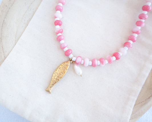 Side view of a necklace with pink and white beads and a gold sardine fish pendant and freshwater pearl bead on a person wearing a white top. The necklace is made with seed beads and freshwater pearls and a big gold sardine fish The sardine fish pendant is made of 18k gold stainless steel. 