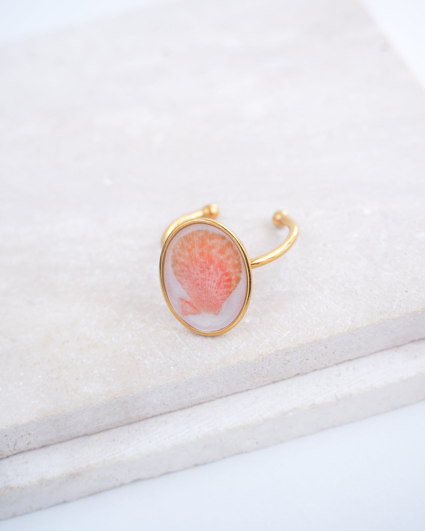 Side view ring with a pink and gold design on a white fabric background. Tiny Scallop Shell Gold Ring on stone displayed. Tiny Coral Pink Scallop Shell Bezel Ring, 18k gold stainless steel, handpicked scallop shell from the beach of Portugal.