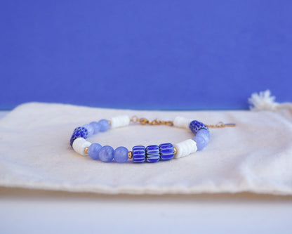 Beaded bracelet with blue and white beads on a blue background. Bracelet with  blue angelite gemstones, dark blue striped beads and white shell beads displayed on a light cotton and blue background.  