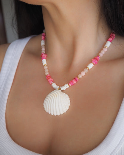 Necklace with pink beads and a white shell pendant on neck model. Necklace with pink and white beads and a shell pendant. A big white cockle shell and a necklace paired with rose quartz gemstone beads, pink stones and white shell beads. The shell is a mediterranean cockle shell from Portugal and is about 4 cm. The color of the shell is ivory.