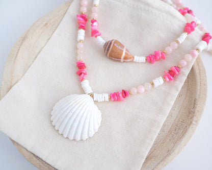 Necklace with pink and white beads and a shell pendant on light cotton displayed. A big white cockle shell and a necklace with a big cone shell paired with rose quartz gemstone beads, pink stones and white shell beads. The shell is a mediterranean cockle shell and Mediterranean Cone Shell from Portugal and is about 4 cm. The color of the shell is ivory and brown.