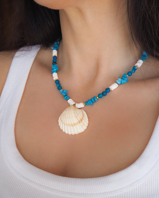 Model wearing a necklace with a big clam shell paired with agate gemstone beads, turquoise stones and white shell beads. The shell is a mediterranean cockle shell from Portugal and is about 4 cm. The color of the shell is ivory bege.