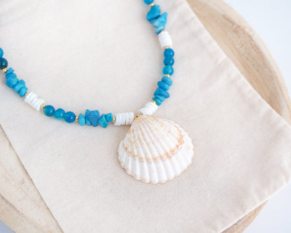 Necklace with blue beads and a shell pendant on a beige fabric background