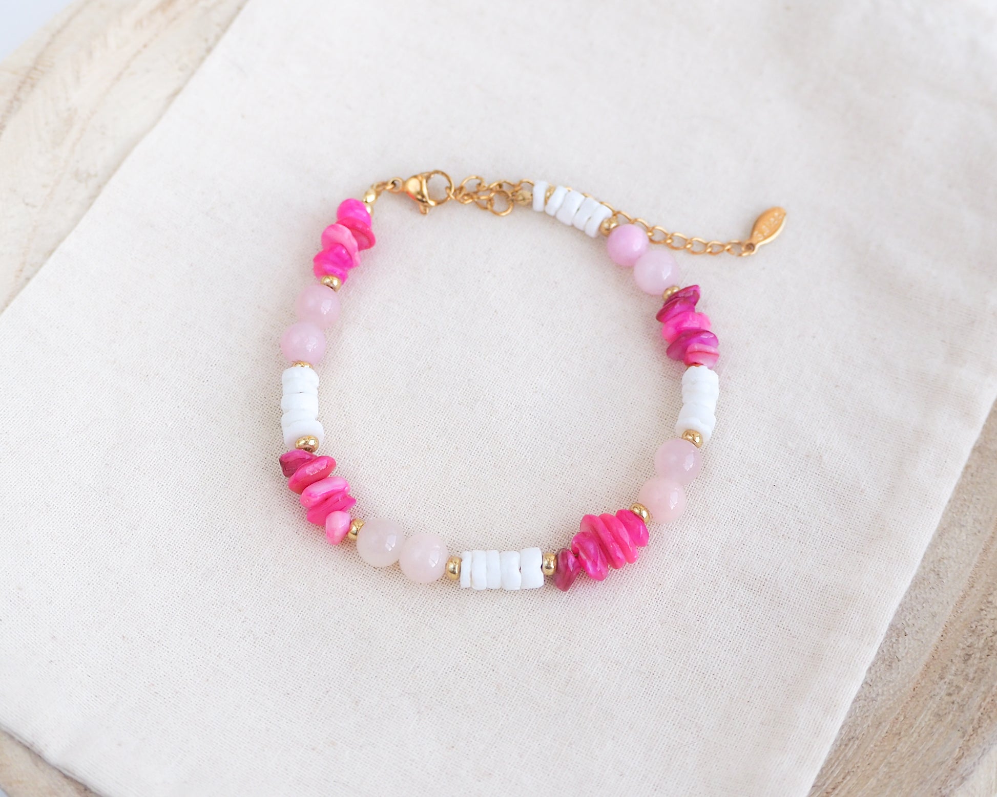 Beaded bracelet with pink, white, and gold beads on a light background. Made with rose quartz, pink stones, white shell beads. The color is pink combined with white. 