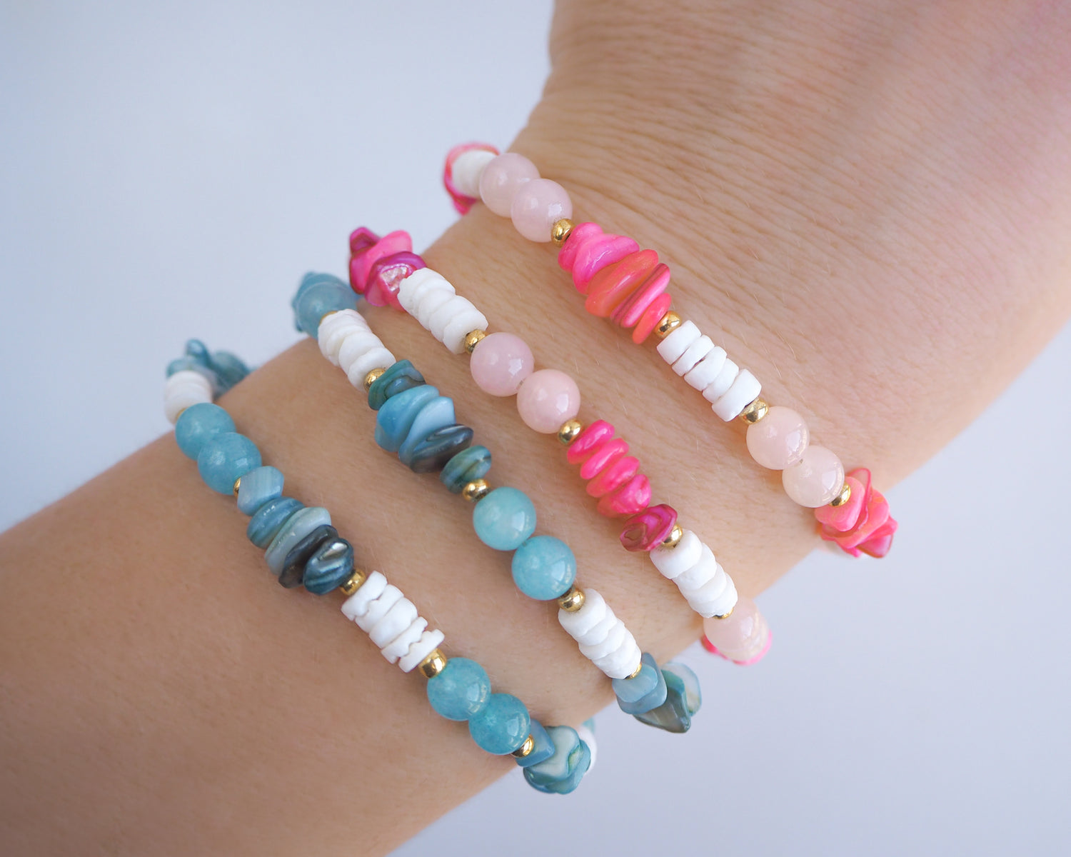 Colorful beaded bracelets on a wrist against a light background. Model wearing seaside bracelets on wrist. Made with rose quartz, pink stones, white shell beads, turquoise stones and aquamarine gemstone beads. The color is pink and turquoise combined with white. 