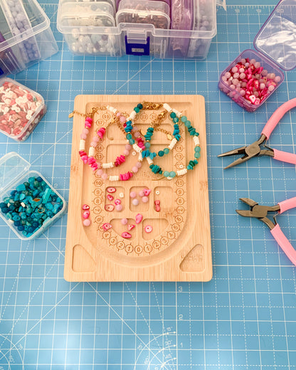 Beadboard with jewelry-making project on a blue cutting mat with tools and containers.