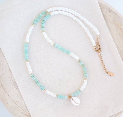 A cowrie necklace with soft green stone beads, jade beads and white shell beads. The center piece of this necklace is a Northern Cowrie Shell, handpicked from the beach of Portugal. The shell is white and about 1 cm. 