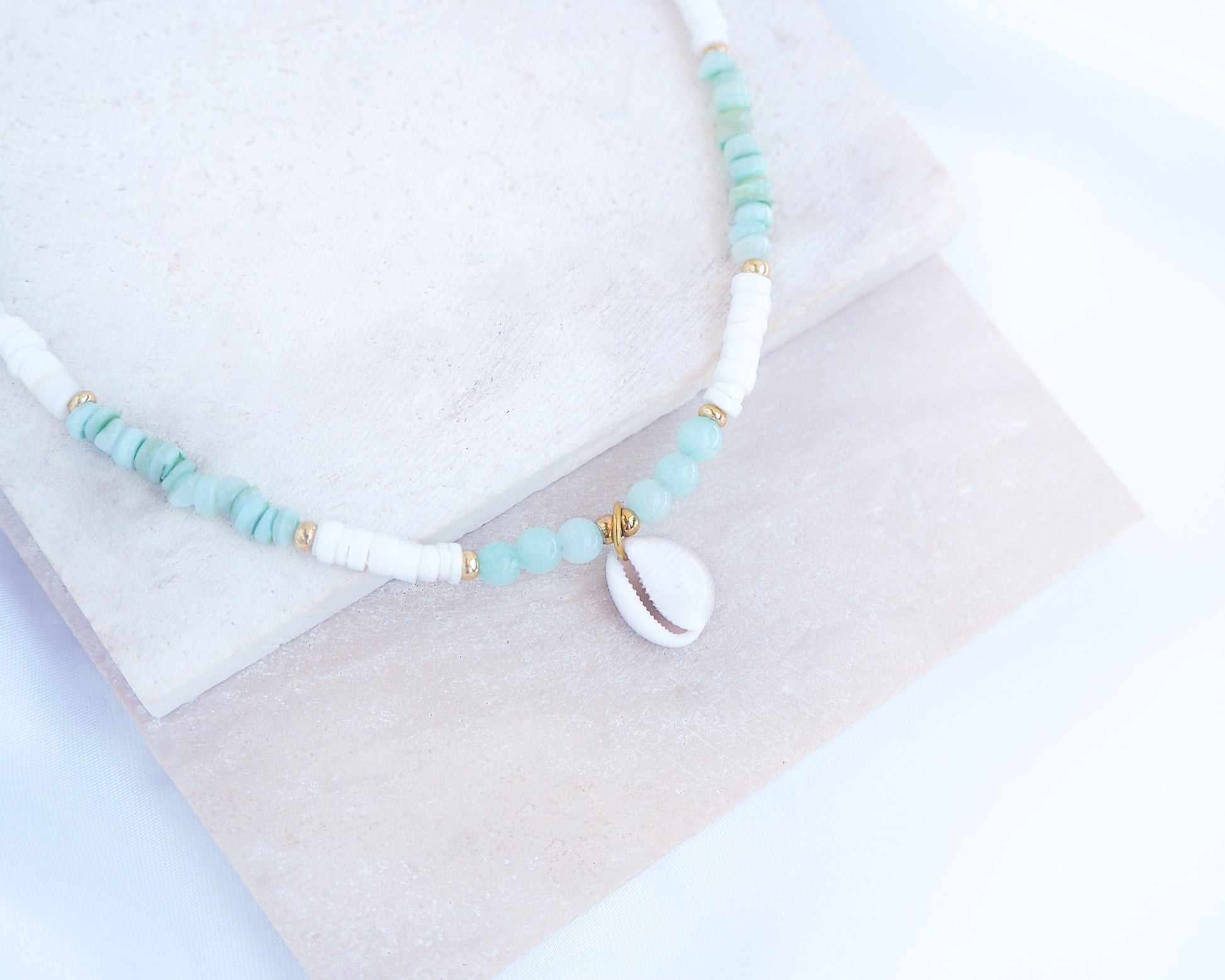 Necklace with turquoise and white beads on a light background. a cowrie necklace with soft green stone beads, jade beads and white shell beads. The center piece of this necklace is a Northern Cowrie Shell, handpicked from the beach of Portugal. The shell is white and about 1 cm. 