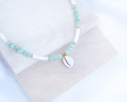 Necklace with turquoise and white beads on a light background. a cowrie necklace with soft green stone beads, jade beads and white shell beads. The center piece of this necklace is a Northern Cowrie Shell, handpicked from the beach of Portugal. The shell is white and about 1 cm. 