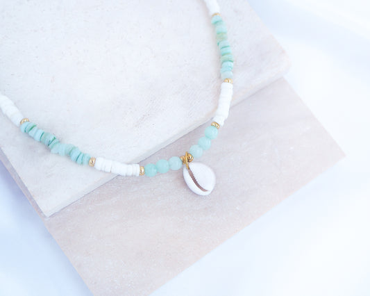 Necklace with turquoise and white beads on a light background. a cowrie necklace with soft green stone beads, jade beads and white shell beads. The center piece of this necklace is a Northern Cowrie Shell, handpicked from the beach of Portugal. The shell is white and about 1 cm. 