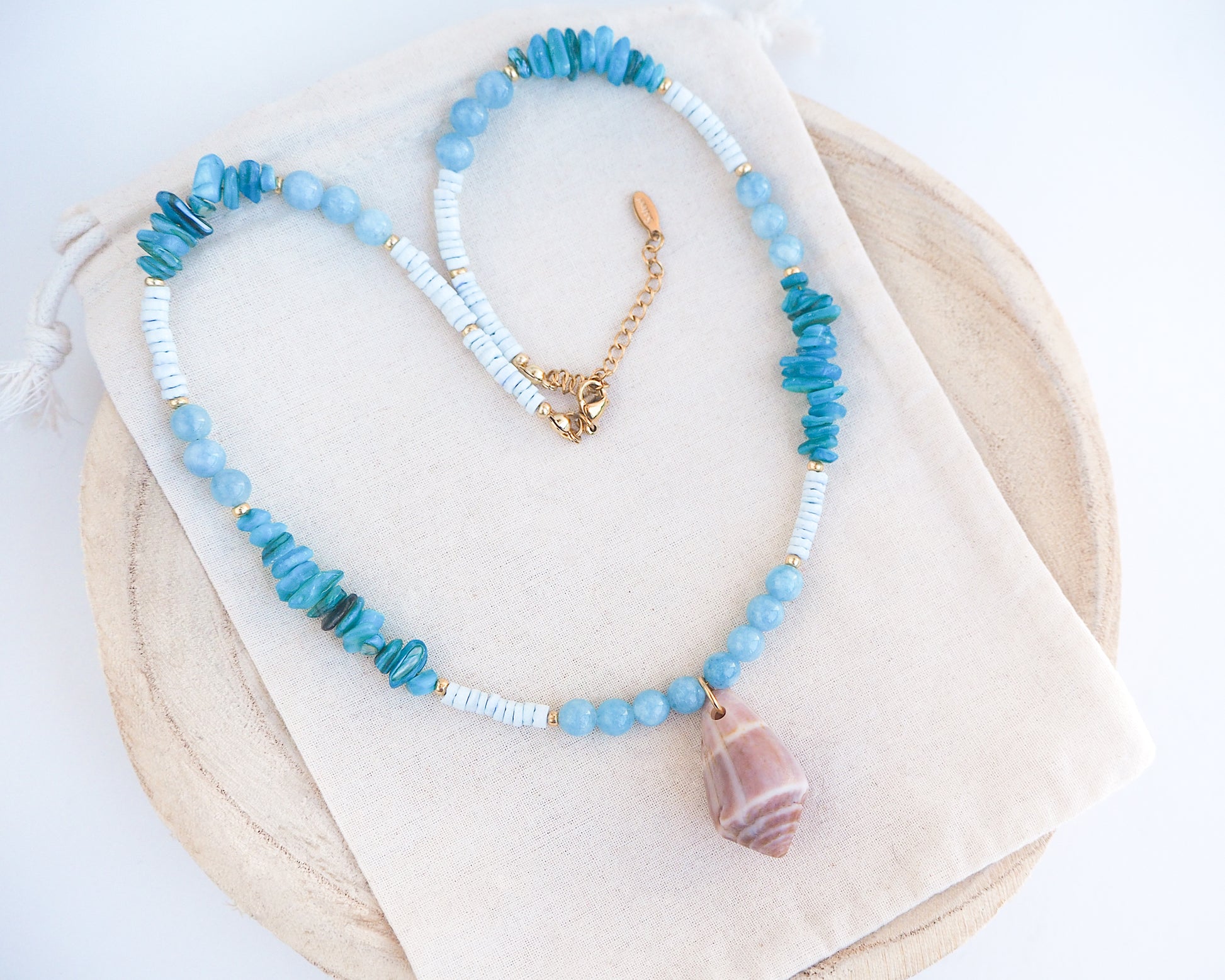 Necklace with blue and white beads and a large cone shell pendant on a light background. A necklace with a mediterranean cone shell paired with aquamarine gemstone beads and white shell beads. The shell is a mediterranean cone shell from Portugal and is about 4 cm. The color of the shell is brown.