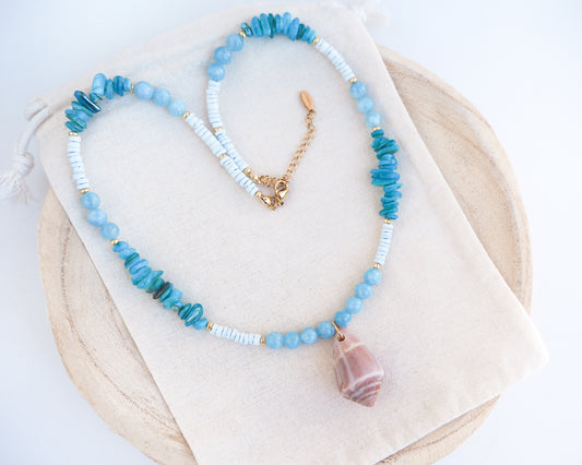Necklace with blue and white beads and a large cone shell pendant on a light background. A necklace with a mediterranean cone shell paired with aquamarine gemstone beads and white shell beads. The shell is a mediterranean cone shell from Portugal and is about 4 cm. The color of the shell is brown.