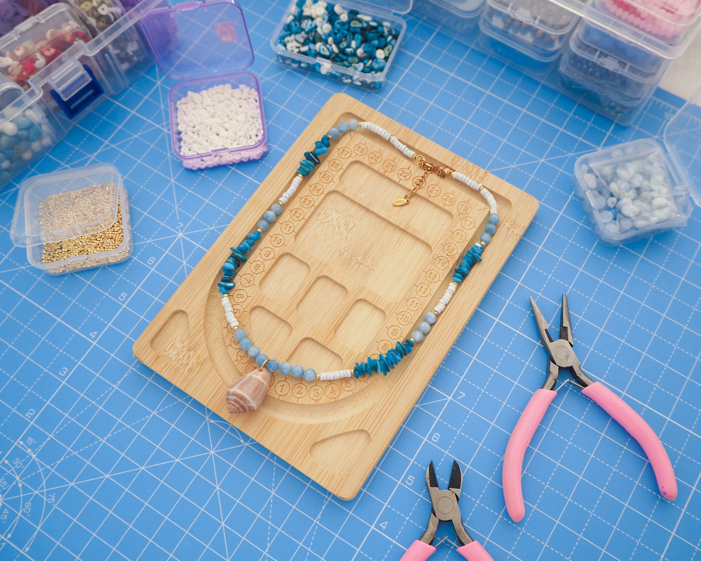 Jewelry-making setup with beads, tools, and a necklace on a blue grid surface