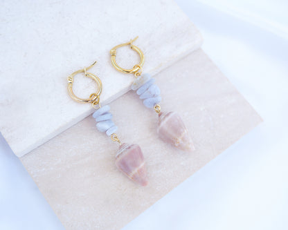 Gold Cone Shell Blue Gemstone Earrings displayed on light stone. Gold earring hoops with real Mediterranean Cone Shells from Portugal and blue agate gemstones. Made with 14k gold stainless steel hoop earrings.   