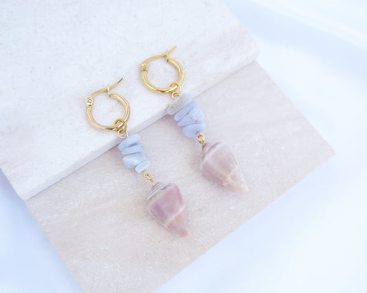 Gold Cone Shell Blue Gemstone Earrings displayed on light stone. Gold earring hoops with real Mediterranean Cone Shells from Portugal and blue agate gemstones. Made with 14k gold stainless steel hoop earrings.   