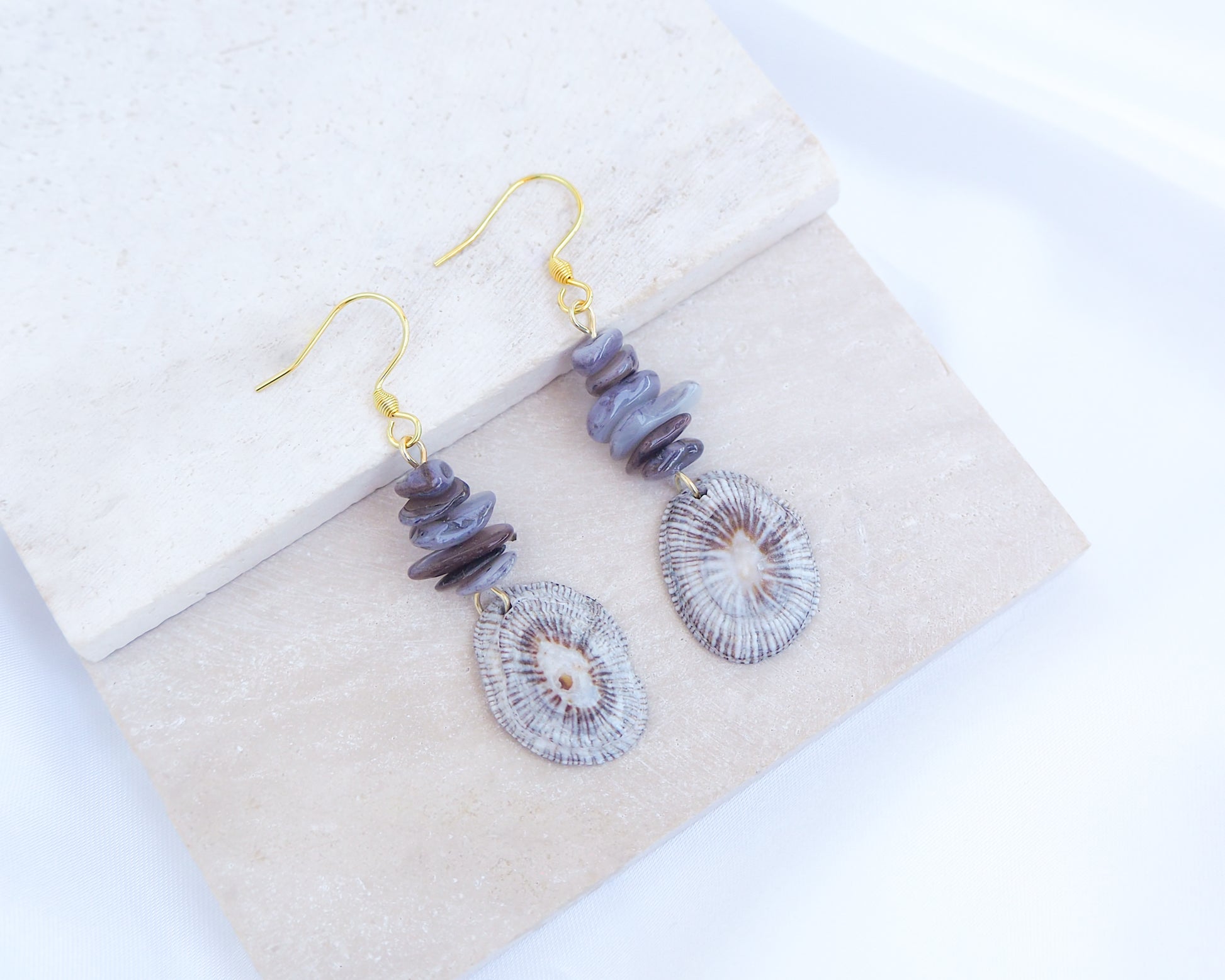 Gold hoop earring with shell and dark stones on display. Gold Striped Limpet Shell Dark Grey Stone Drop Earrings. Gold hoops with real shells from Portugal. Made with 14k gold stainless steel hoop earrings.   