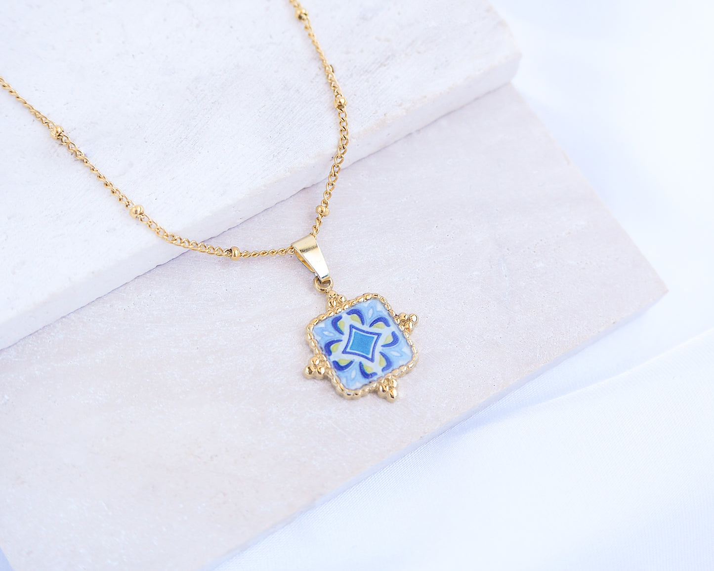 Gold necklace with a blue pendant on a light background
