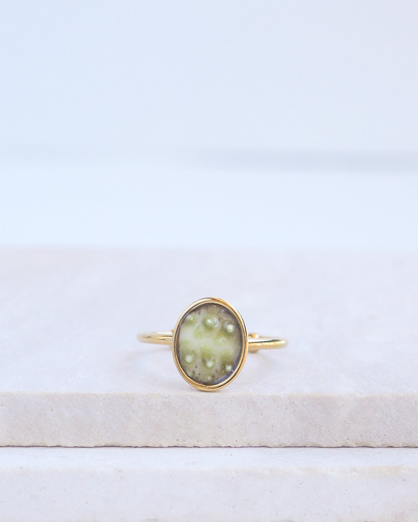 Green Sea Urchin Shell Ring on display. Made with a handpicked piece of kaki green sea urchin shell from Portugal set in a 18k gold stainless steel bezel. It's an adjustable ring 