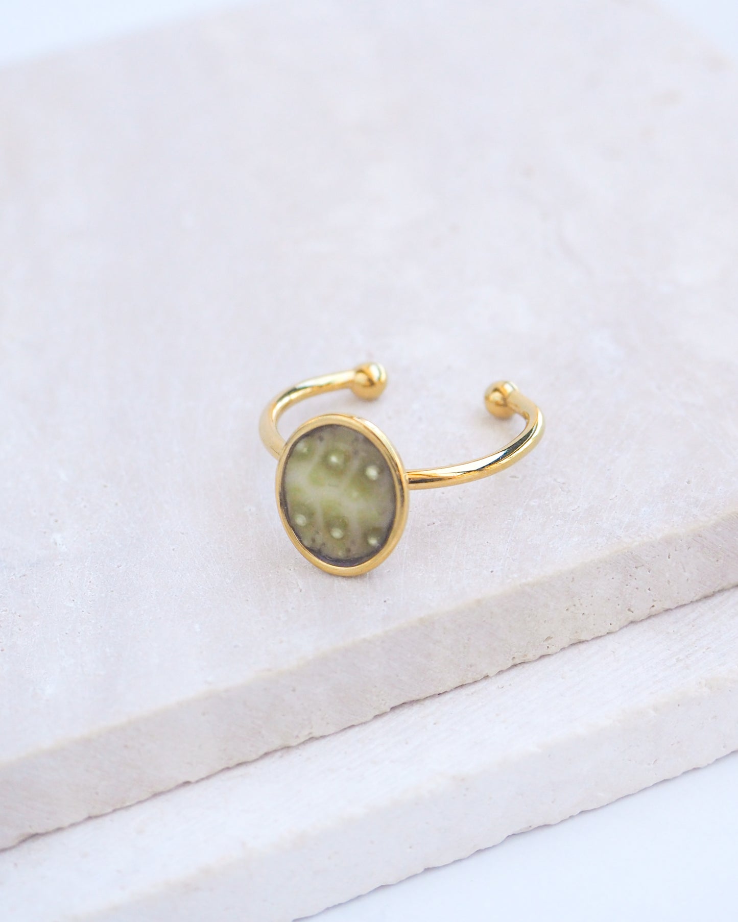 Side view of Green Sea Urchin Shell Ring on display. Made with a handpicked piece of kaki green sea urchin shell from Portugal set in a 18k gold stainless steel bezel. It's an adjustable ring 