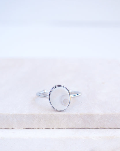 Silver bezel ring with a tiny ivory white shiva eye on stone displayed with light background. White Eye of Saint Lucia Gold Ring on stone displayed, silver stainless steel shiva eye operculum, Saint Lucy Eye, operculum pendant