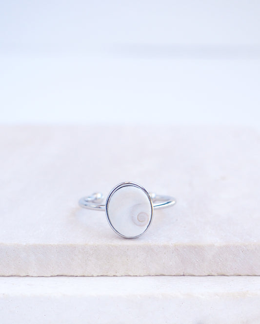 Silver bezel ring with a tiny ivory white shiva eye on stone displayed with light background. White Eye of Saint Lucia Gold Ring on stone displayed, silver stainless steel shiva eye operculum, Saint Lucy Eye, operculum pendant
