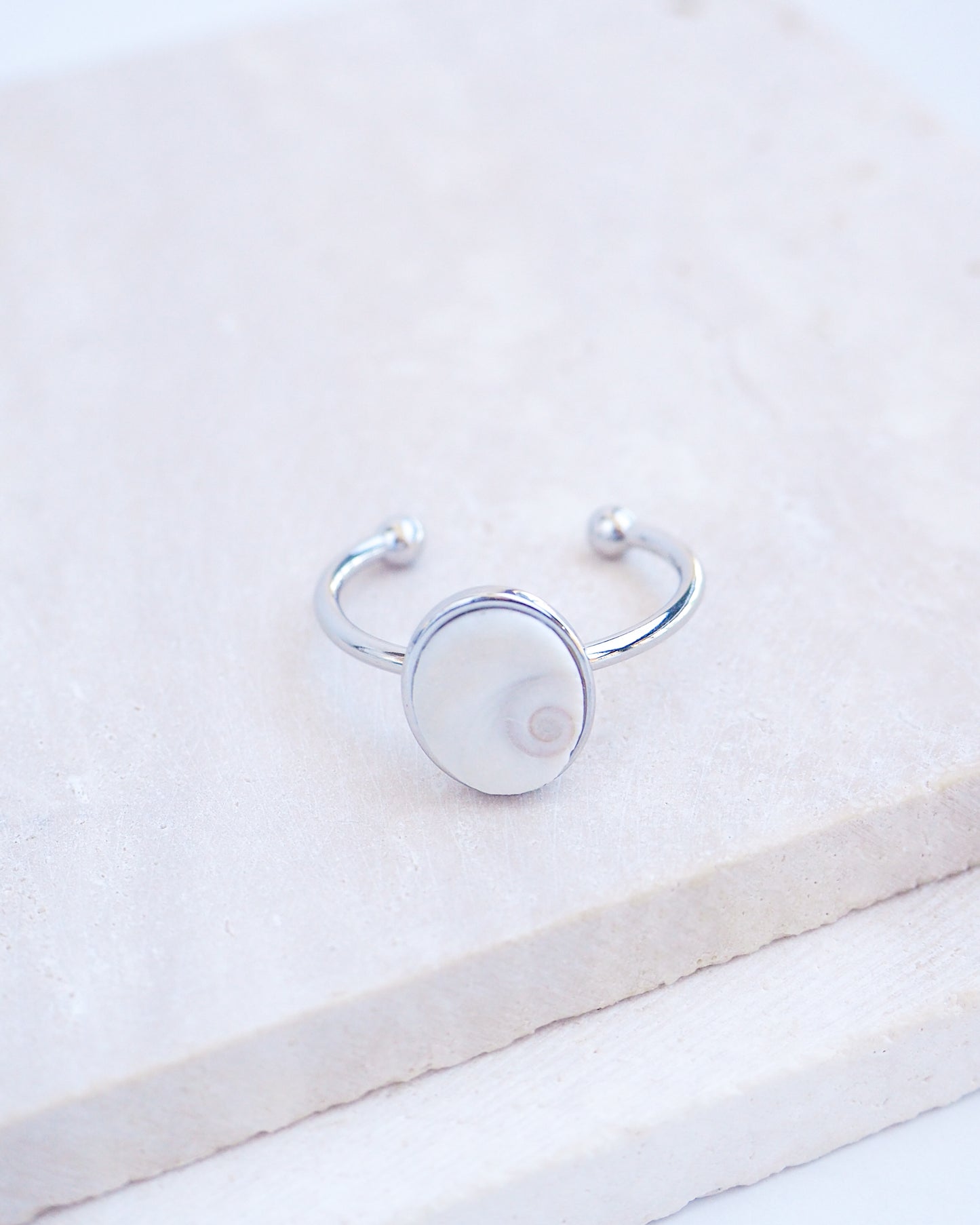 Side view of Silver bezel ring with a tiny ivory white shiva eye on stone displayed with light background. White Eye of Saint Lucia Gold Ring on stone displayed, silver stainless steel shiva eye operculum, Saint Lucy Eye, operculum pendant