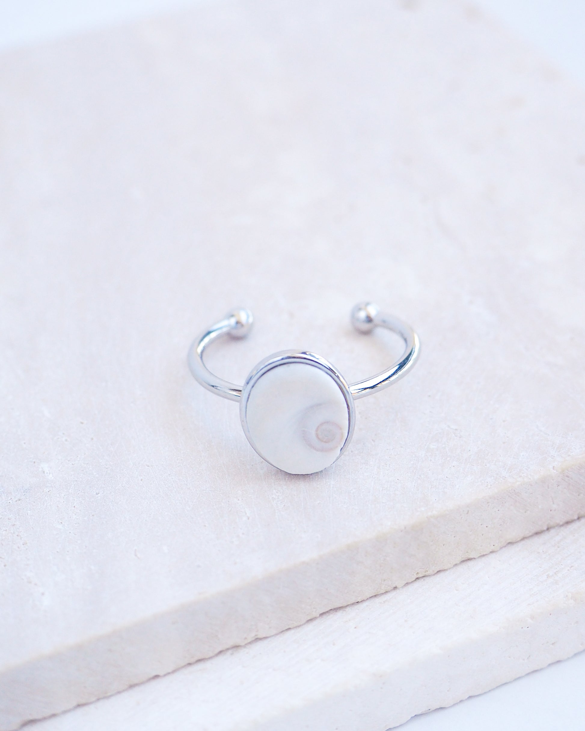 Side view of Silver bezel ring with a tiny ivory white shiva eye on stone displayed with light background. White Eye of Saint Lucia Gold Ring on stone displayed, silver stainless steel shiva eye operculum, Saint Lucy Eye, operculum pendant