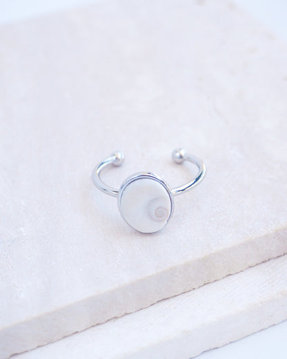 Side view of Silver bezel ring with a tiny ivory white shiva eye on stone displayed with light background. White Eye of Saint Lucia Gold Ring on stone displayed, silver stainless steel shiva eye operculum, Saint Lucy Eye, operculum pendant