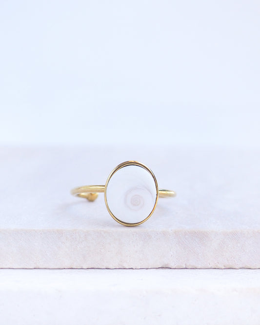Front view of Gold bezel ring with a white shiva eye on stone displayed with light background. White Eye of Saint Lucia Gold Ring on stone displayed, 18k gold stainless steel shiva eye operculum, Saint Lucy Eye, operculum pendant