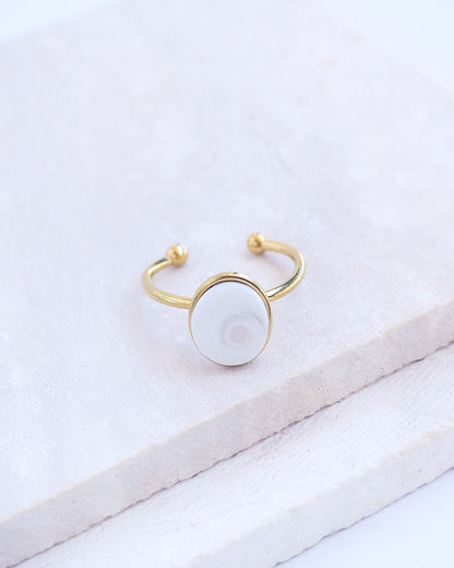 Side view of Gold bezel ring with a white shiva eye on stone displayed with light background. White Eye of Saint Lucia Gold Ring on stone displayed, 18k gold stainless steel shiva eye operculum, Saint Lucy Eye, operculum pendant
