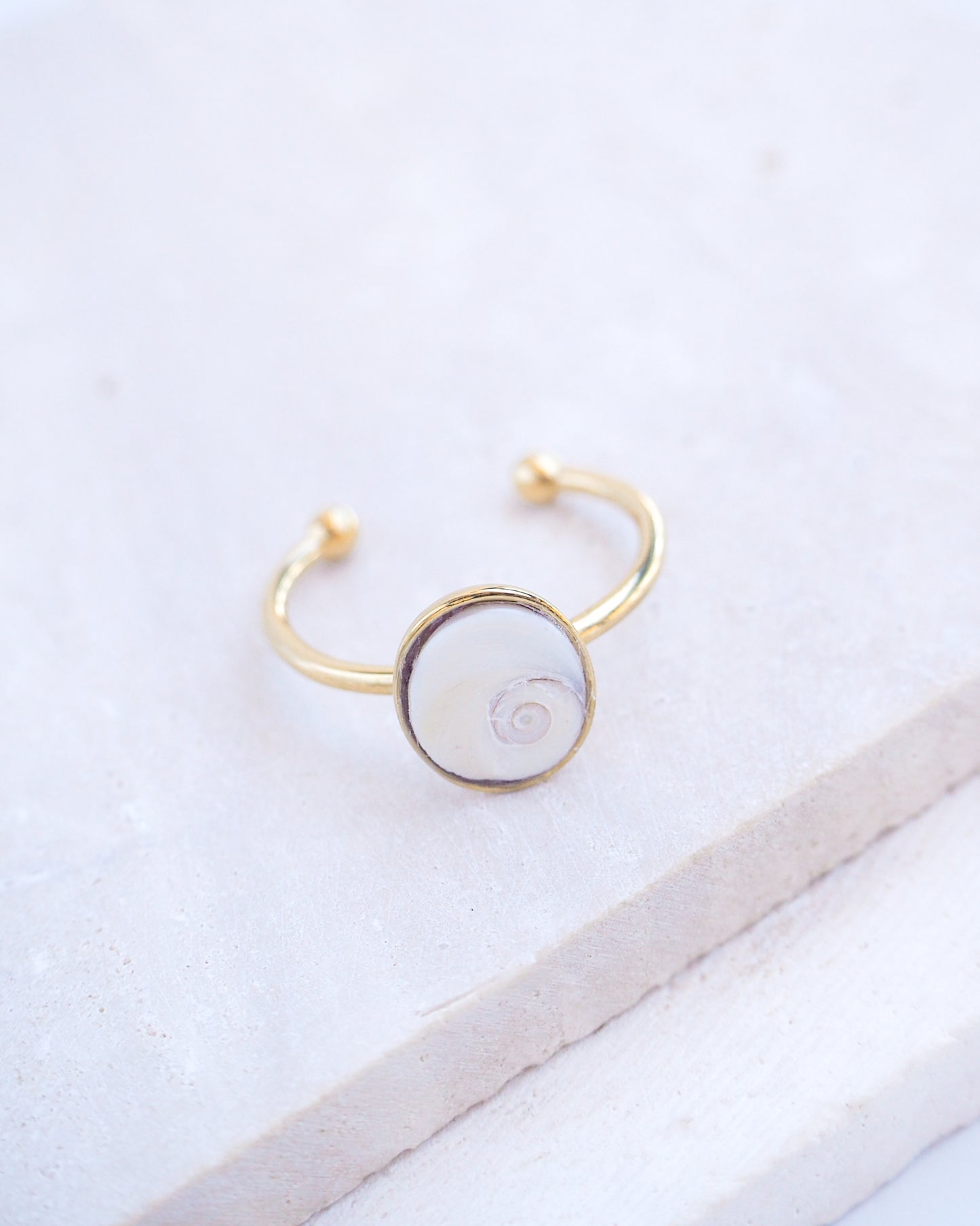 Side view of Gold bezel ring with a tiny ivory white shiva eye on stone displayed with light background. White Eye of Saint Lucia Gold Ring on stone displayed, 18k gold stainless steel shiva eye operculum, Saint Lucy Eye, operculum pendant