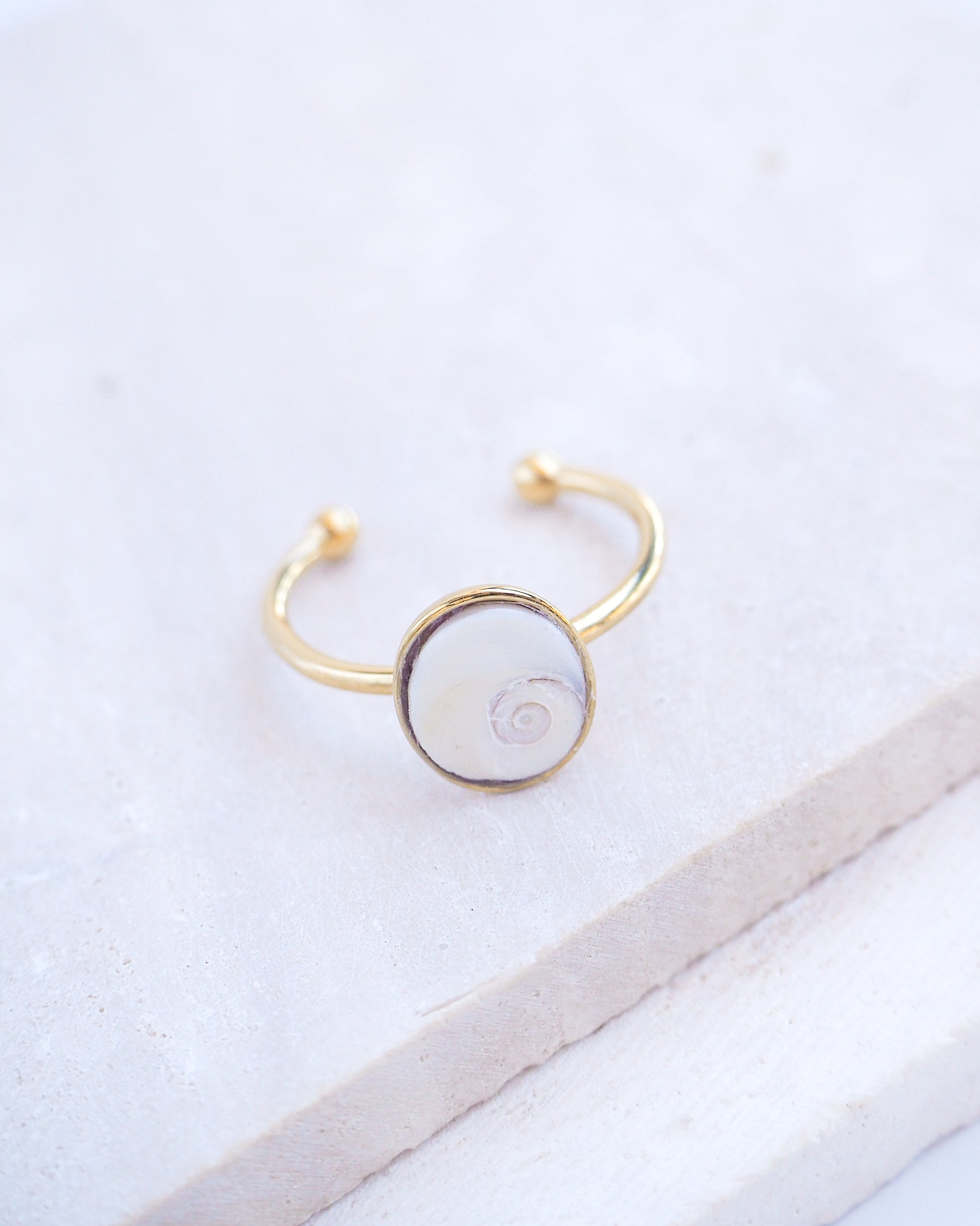 Side view of Gold bezel ring with a tiny ivory white shiva eye on stone displayed with light background. White Eye of Saint Lucia Gold Ring on stone displayed, 18k gold stainless steel shiva eye operculum, Saint Lucy Eye, operculum pendant