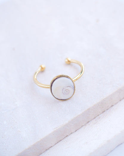 Side view of Gold bezel ring with a tiny ivory white shiva eye on stone displayed with light background. White Eye of Saint Lucia Gold Ring on stone displayed, 18k gold stainless steel shiva eye operculum, Saint Lucy Eye, operculum pendant