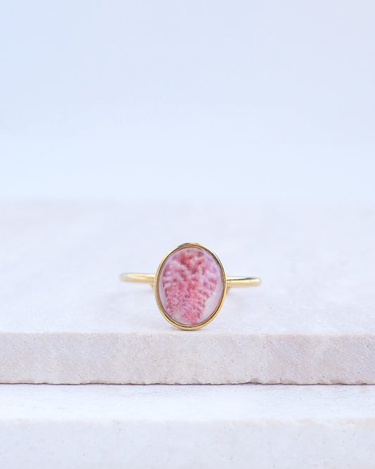 Ring with a pink and gold design on a white fabric background. Tiny Scallop Shell Gold Ring on stone displayed. Tiny Pink Scallop Shell Bezel Ring, 18k gold stainless steel, handpicked scallop shell from the beach of Portugal.