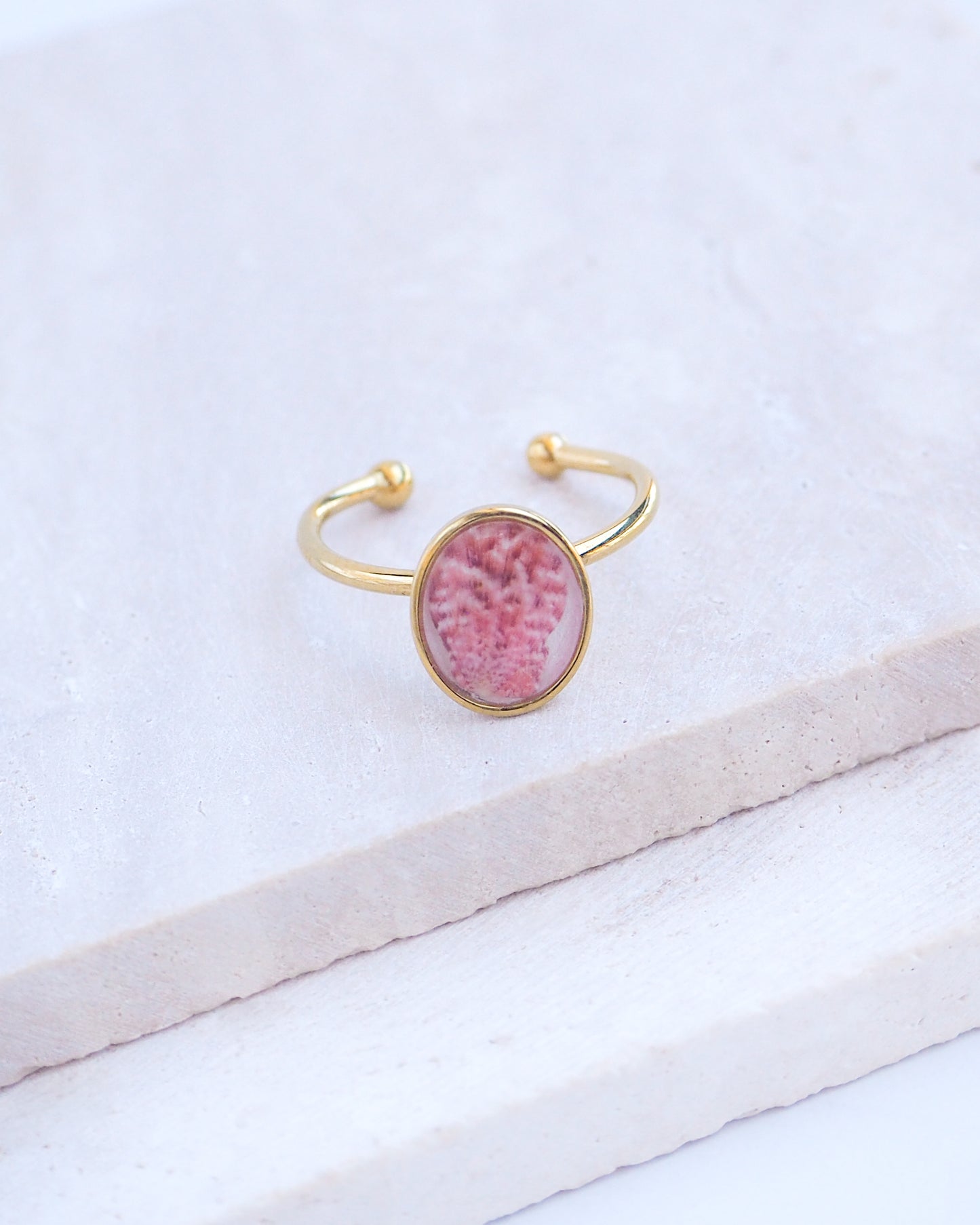 Ring with a pink and gold design on a white fabric background. Tiny Scallop Shell Gold Ring on stone displayed. Tiny Pink Scallop Shell Bezel Ring, 18k gold stainless steel, handpicked scallop shell from the beach of Portugal.